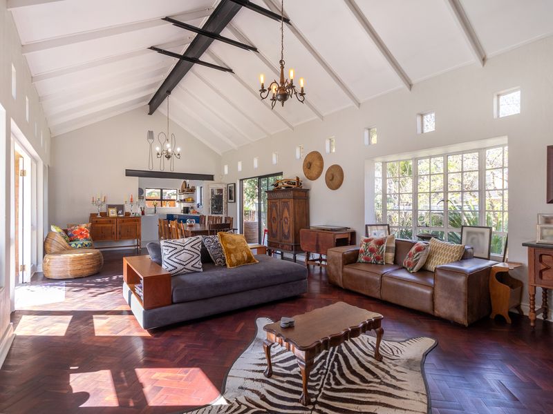 Spacious open-plan living area featuring a high vaulted ceiling with exposed beams, elegant herringbone parquet flooring, and abundant natural light through large windows.