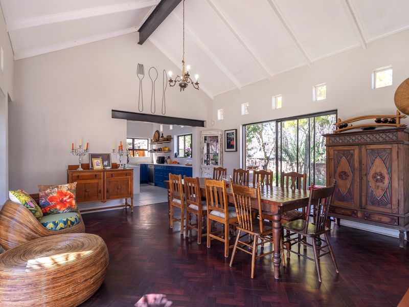 Spacious open-plan living and dining area featuring vaulted ceilings, exposed structural beams, rich herringbone timber flooring, and large sliding doors opening to the garden.
