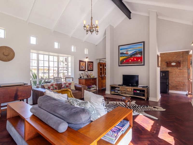 Spacious living room featuring a high vaulted ceiling with exposed beams, elegant herringbone parquet flooring, and a characterful exposed brick accent wall.