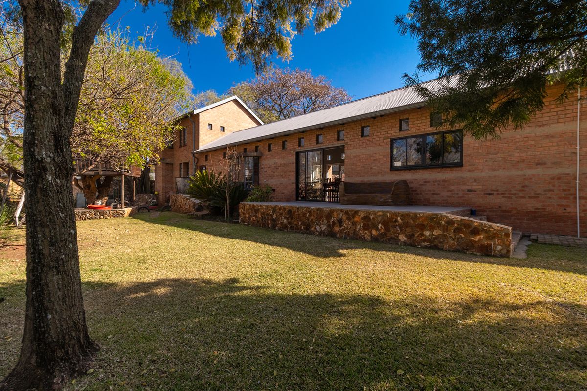 A rear view of the house featuring an exposed brick facade, a stone-clad patio, and a well-maintained garden area.