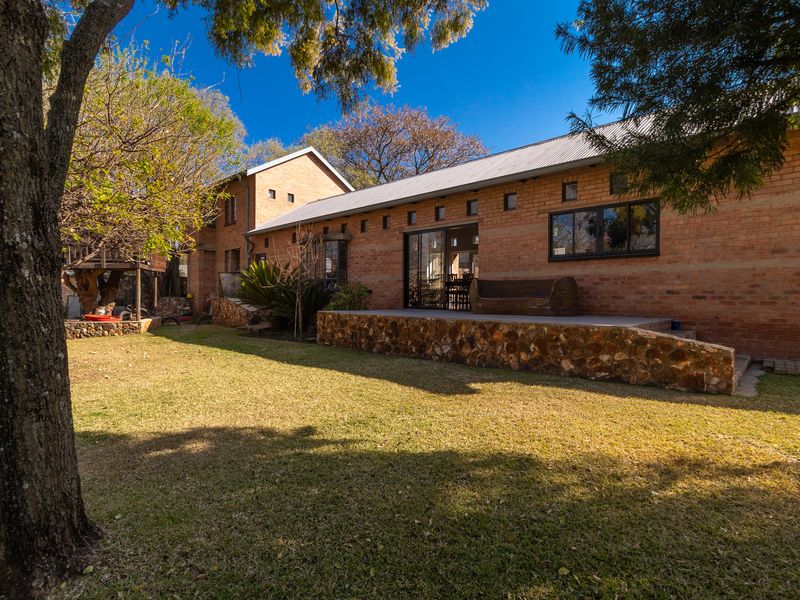 A rear view of the house featuring an exposed brick facade, a stone-clad patio, and a well-maintained garden area.