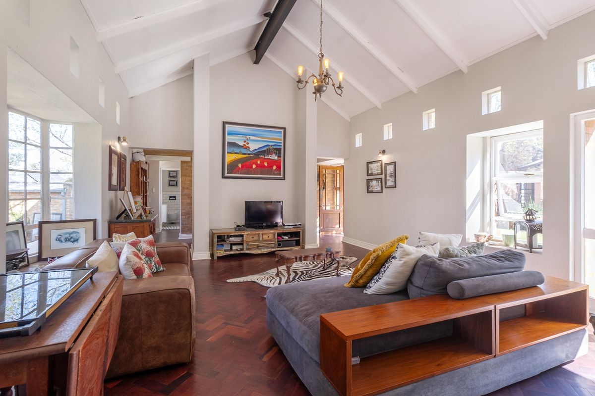 Spacious living room featuring a high vaulted ceiling with exposed beams, elegant herringbone timber flooring, and abundant natural light from clerestory and bay windows.