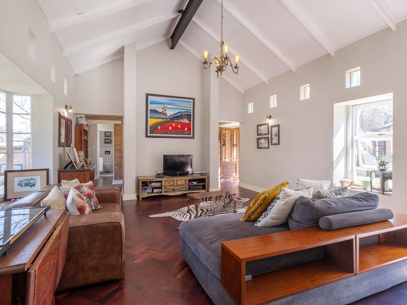 Spacious living room featuring a high vaulted ceiling with exposed beams, elegant herringbone timber flooring, and abundant natural light from clerestory and bay windows.