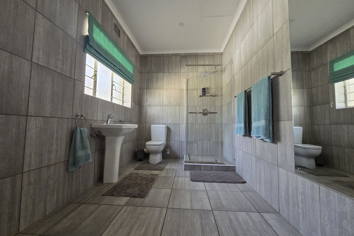 A modern bathroom featuring floor-to-ceiling neutral tiling, a pedestal basin, a glass-enclosed shower, and a wall-mounted mirror.
