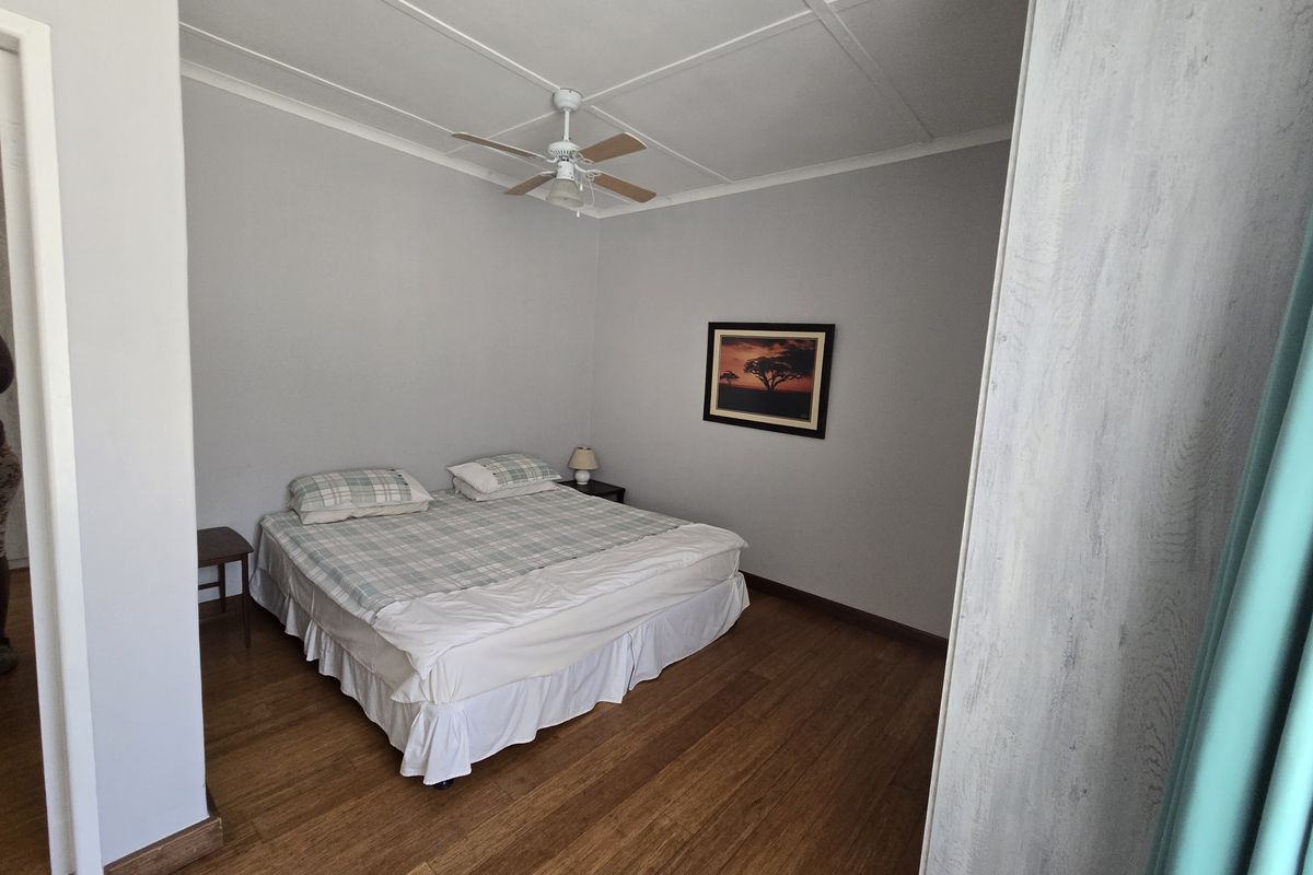 A bedroom featuring timber flooring, a ceiling fan, and neutral wall finishes.