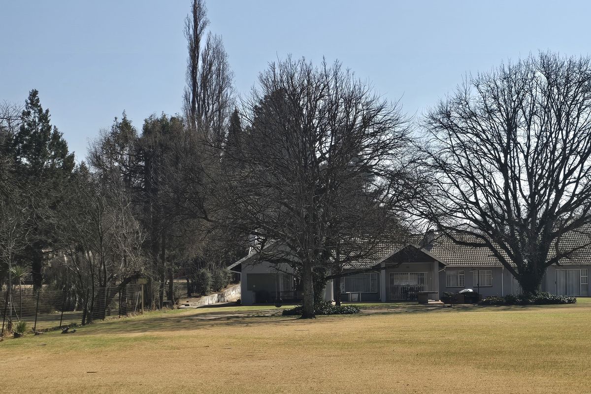 A view of the property's rear exterior, featuring a large open lawn, mature trees, and the main dwelling structure with a tiled roof.