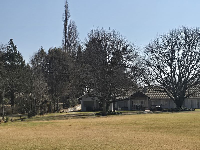 A view of the property's rear exterior, featuring a large open lawn, mature trees, and the main dwelling structure with a tiled roof.