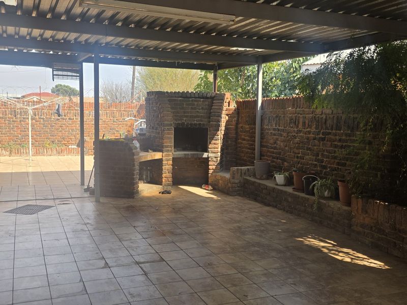 Covered outdoor patio area featuring a built-in brick braai, tiled flooring, and a brick boundary wall with a raised planter.