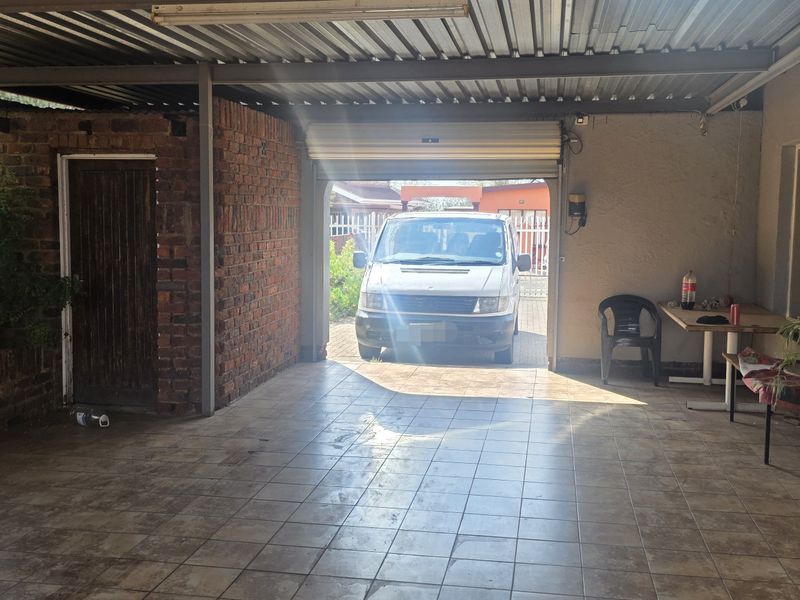 A spacious, covered garage area featuring tiled flooring, exposed brick accents, and a functional roller shutter door, providing secure parking or utility space.