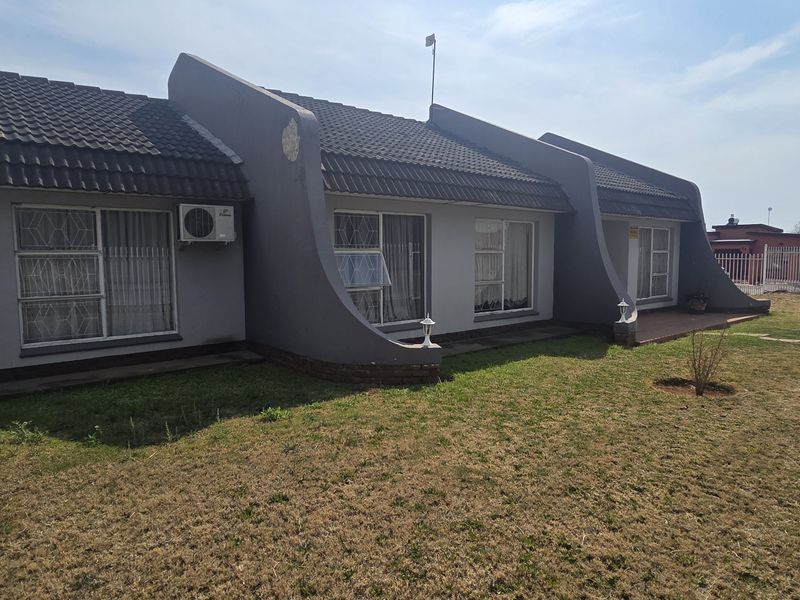 Rear view of the property featuring a tiled roof, concrete architectural features, sliding glass doors, and a private garden area with perimeter fencing.