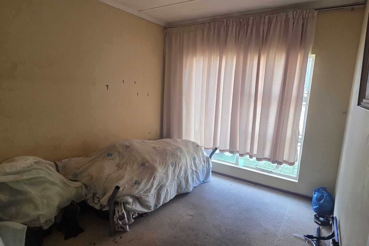 A bedroom featuring carpeted flooring and a large window with curtain tracks, requiring cosmetic updates to the walls and flooring.