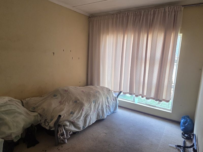 A bedroom featuring carpeted flooring and a large window with curtain tracks, requiring cosmetic updates to the walls and flooring.