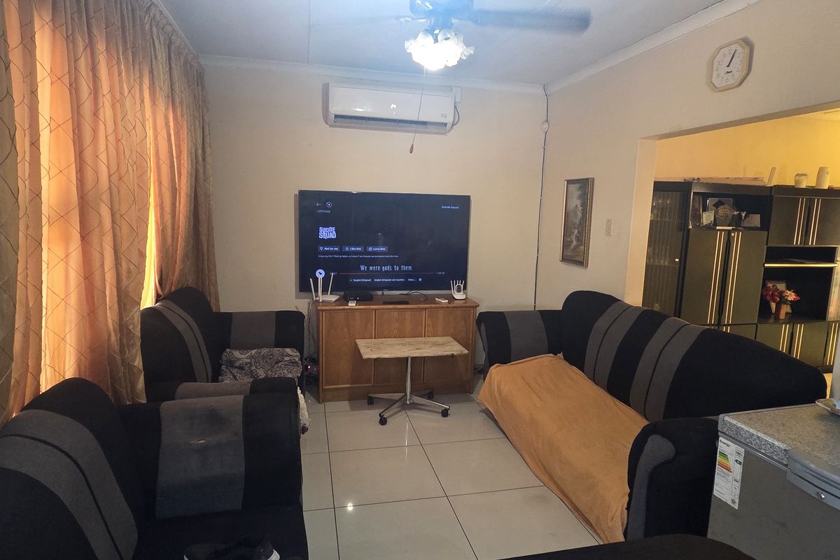 A living room featuring tiled flooring, a ceiling fan, and a wall-mounted air conditioning unit, with an open transition to an adjacent space.