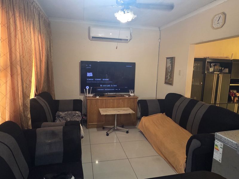 A living room featuring tiled flooring, a ceiling fan, and a wall-mounted air conditioning unit, with an open transition to an adjacent space.