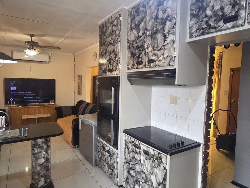 Open-plan living and kitchen area featuring tiled flooring, built-in oven, electric hob, extractor fan, and ceiling fan.