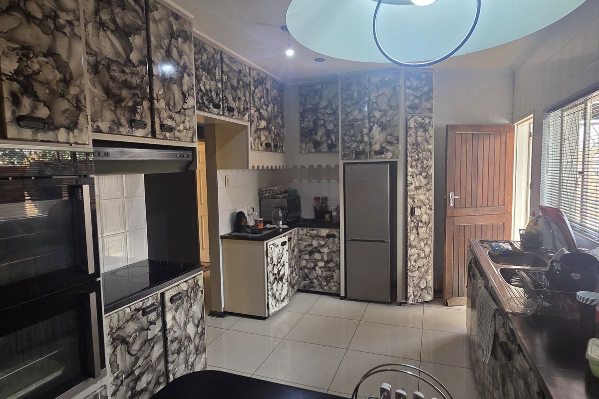 A functional kitchen featuring tiled flooring, built-in oven, extractor fan, and extensive cabinetry with a dated patterned finish.