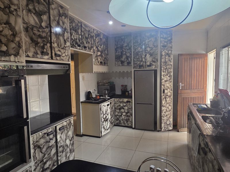 A functional kitchen featuring tiled flooring, built-in oven, extractor fan, and extensive cabinetry with a dated patterned finish.