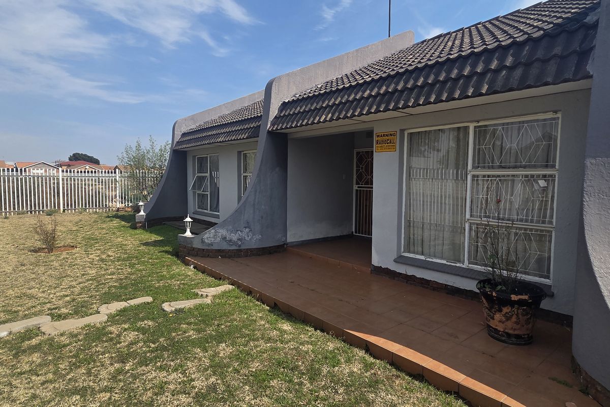 Rear view of the house featuring a tiled patio, security-fitted windows, and a private garden area with perimeter fencing.