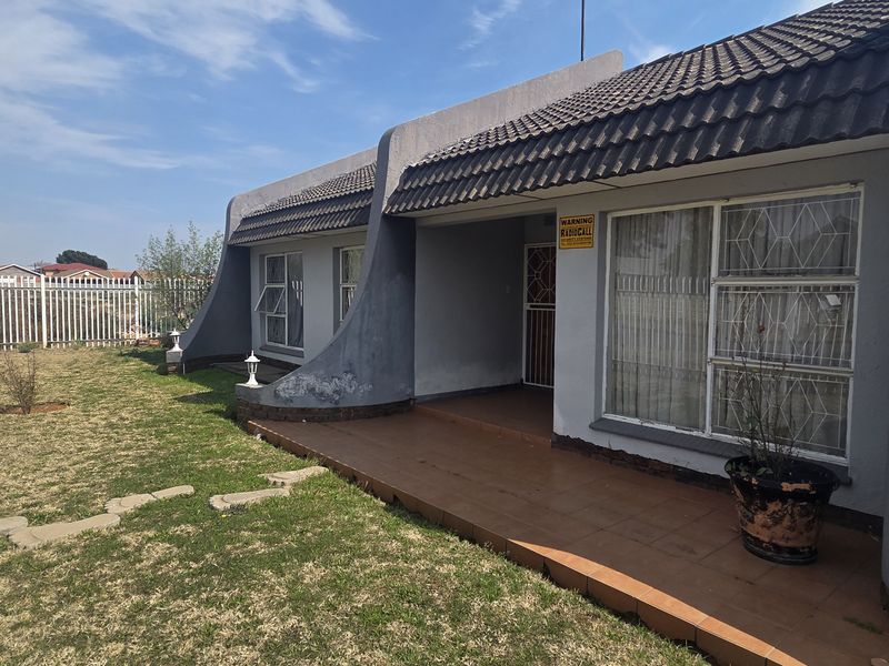 Rear view of the house featuring a tiled patio, security-fitted windows, and a private garden area with perimeter fencing.