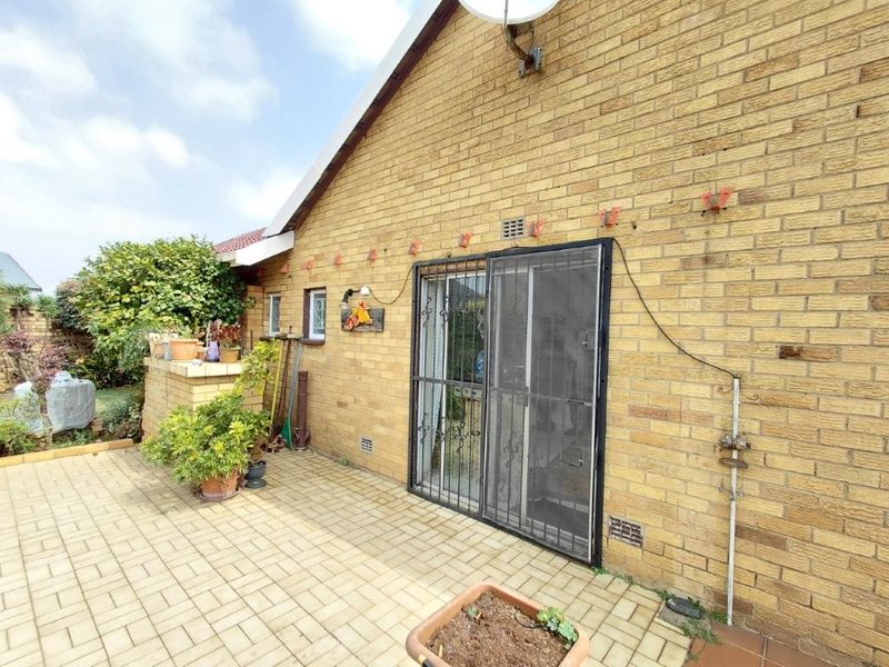 Rear exterior view of the property featuring a paved patio area, brick facade, and a sliding glass door with a security gate.