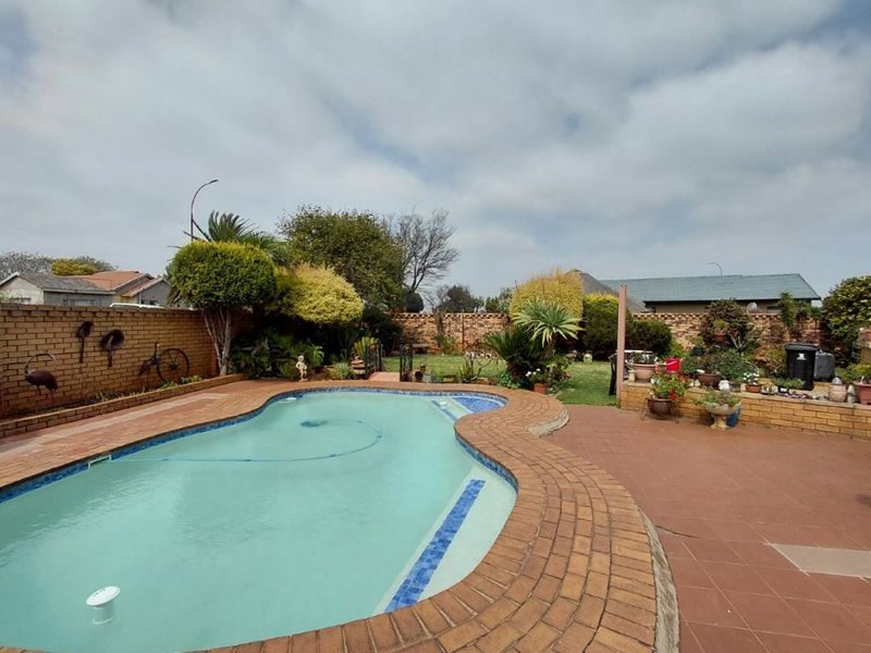 Outdoor pool area featuring a kidney-shaped swimming pool, brick boundary walls, and tiled patio space in a landscaped garden setting.