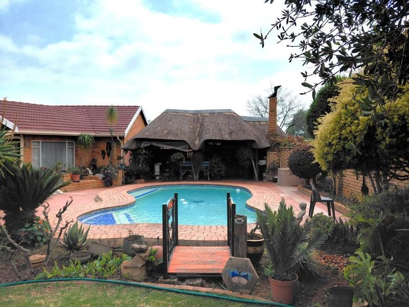 Outdoor pool area featuring a swimming pool, brick paving, and a traditional thatched lapa with a built-in chimney.