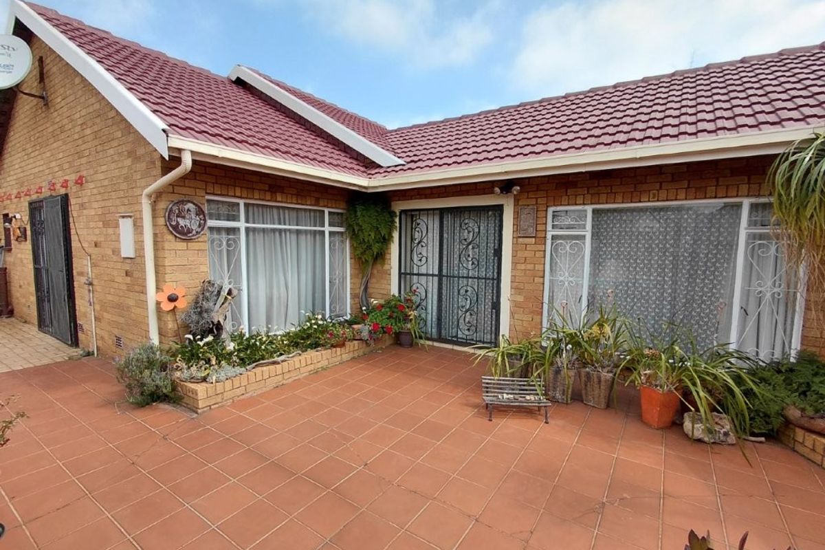 A rear exterior view of a brick house featuring a tiled patio area, security gates, and established garden beds along the building facade.