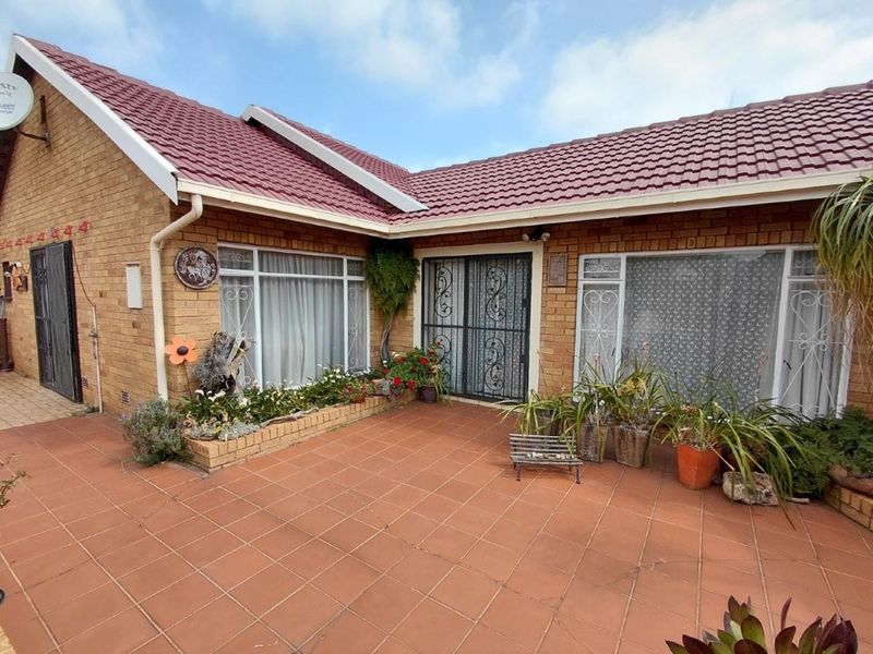 A rear exterior view of a brick house featuring a tiled patio area, security gates, and established garden beds along the building facade.