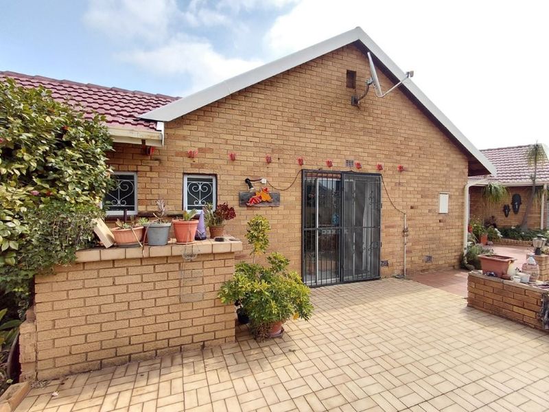 A rear exterior view of a brick house featuring a paved patio area, security gate, and built-in brick planter boxes.
