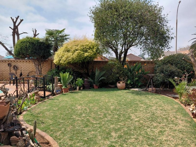 A well-maintained private garden featuring a circular lawn, established trees, and a brick boundary wall with a decorative wrought iron gate.