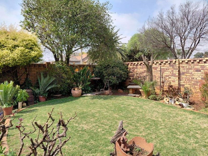 A well-maintained private garden featuring a lush green lawn enclosed by a sturdy face-brick boundary wall and mature landscaping.