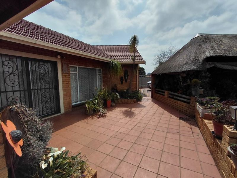 A spacious outdoor patio area featuring tiled flooring, brick construction, and an adjacent thatched roof structure, offering a functional space for outdoor living.