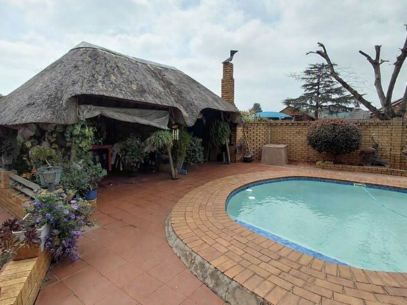 Outdoor entertainment area featuring a thatched lapa with a brick chimney, adjacent to a swimming pool with brick paving and perimeter walling.