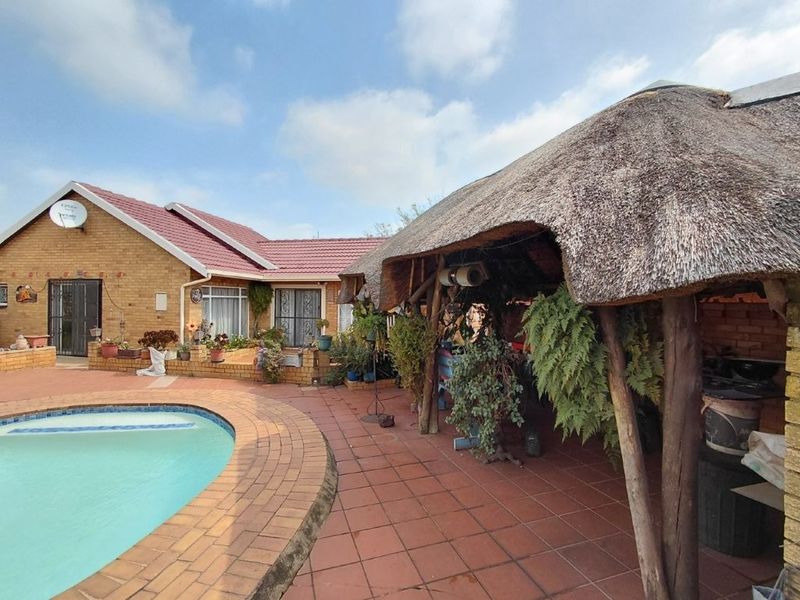 Outdoor entertainment area featuring a swimming pool, paved patio, and a traditional thatched lapa structure adjacent to the main facebrick house.