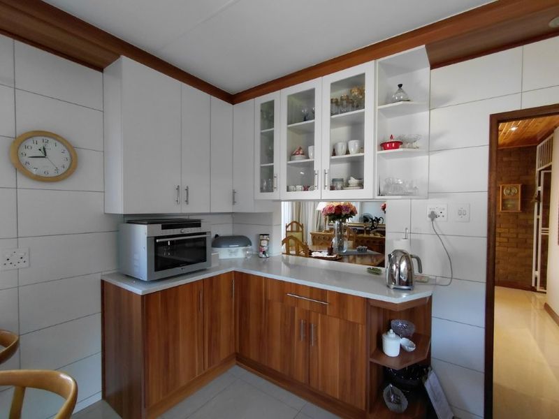 A well-maintained kitchen featuring wood-tone lower cabinetry, white upper cabinets, glass display shelving, and tiled wall finishes.