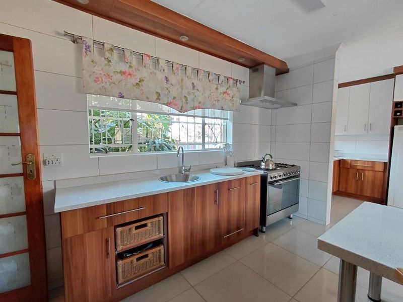 A functional kitchen featuring wood-finish cabinetry, stone countertops, a gas stove with extractor fan, and tiled splashbacks, with an adjacent scullery area.