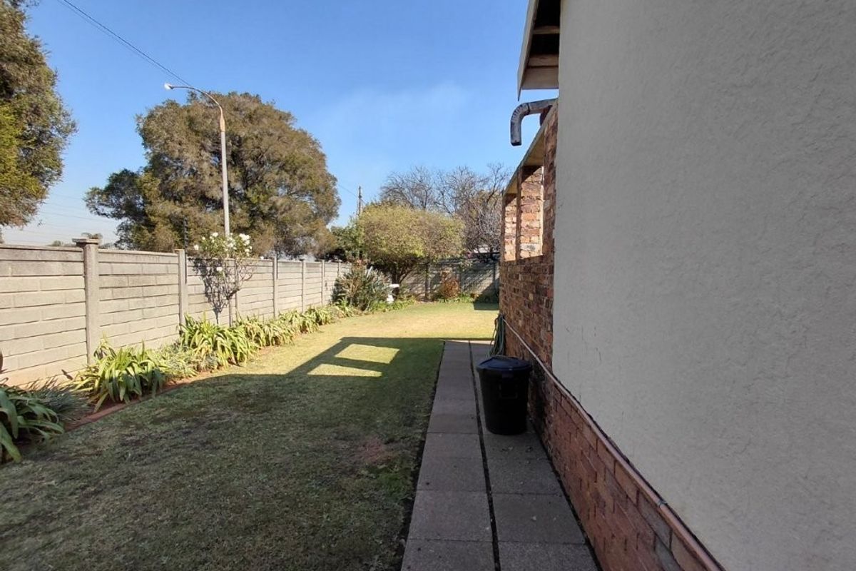 A view of the rear garden featuring a paved walkway, lawn, and precast concrete boundary wall, with visible maintenance required on the building exterior.