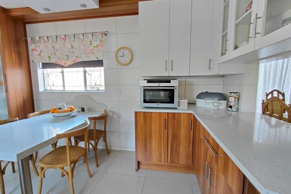 A well-maintained kitchen featuring wood-finish lower cabinetry, white upper cabinets, stone countertops, and a built-in oven with a tiled backsplash.