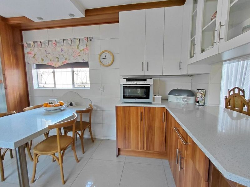 A well-maintained kitchen featuring wood-finish lower cabinetry, white upper cabinets, stone countertops, and a built-in oven with a tiled backsplash.