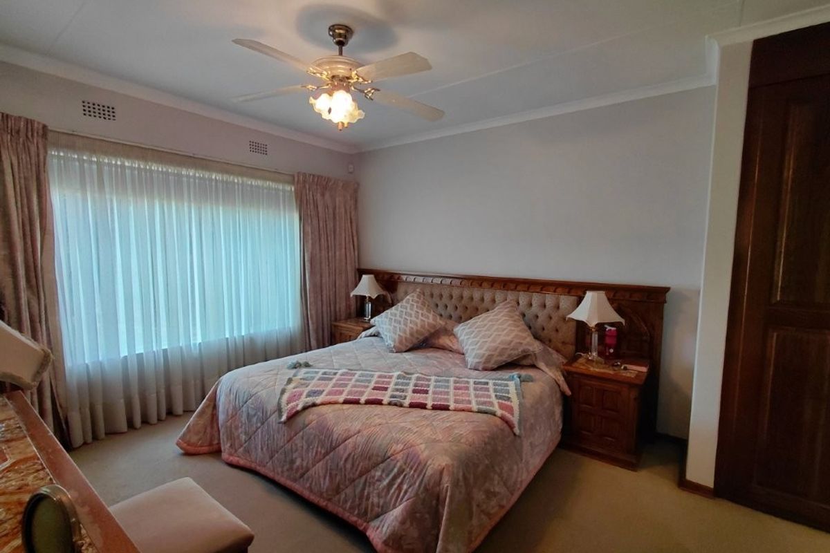 Spacious bedroom featuring neutral carpeting, built-in cupboards, and a ceiling fan, offering a comfortable and functional living space.