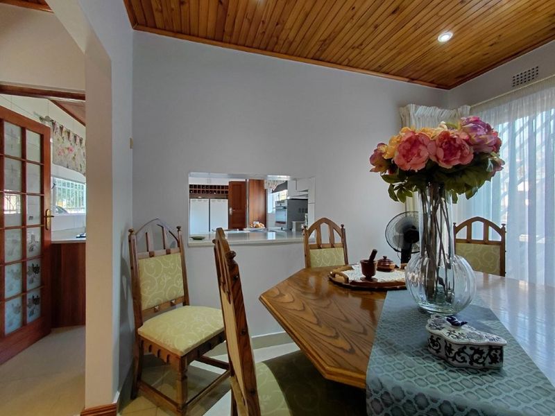 Dining room featuring a timber tongue and groove ceiling, tiled flooring, and a convenient pass-through window connecting to the kitchen area.