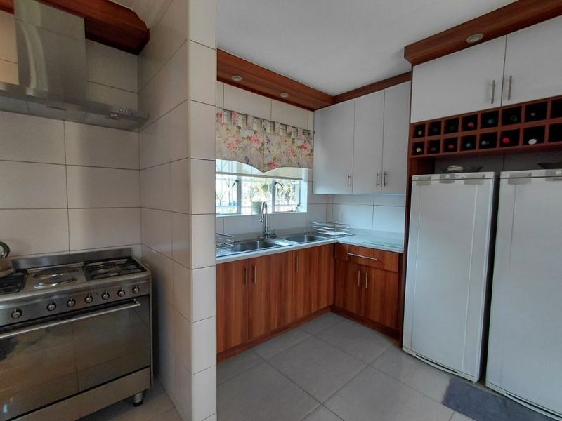A functional kitchen featuring wood-finish lower cabinetry, white upper cabinets, a gas stove with extractor, and a double sink with tiled splashbacks.