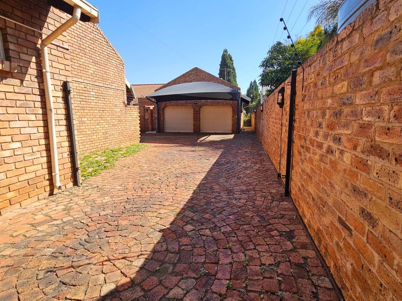 A paved driveway leading to a double garage with a carport, enclosed by brick boundary walls and secured with electric fencing.