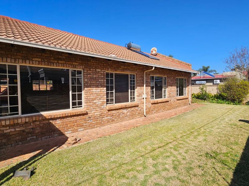 Rear view of the property featuring a face brick facade, tiled roof with solar water heater, paved walkway, and a private lawn area.