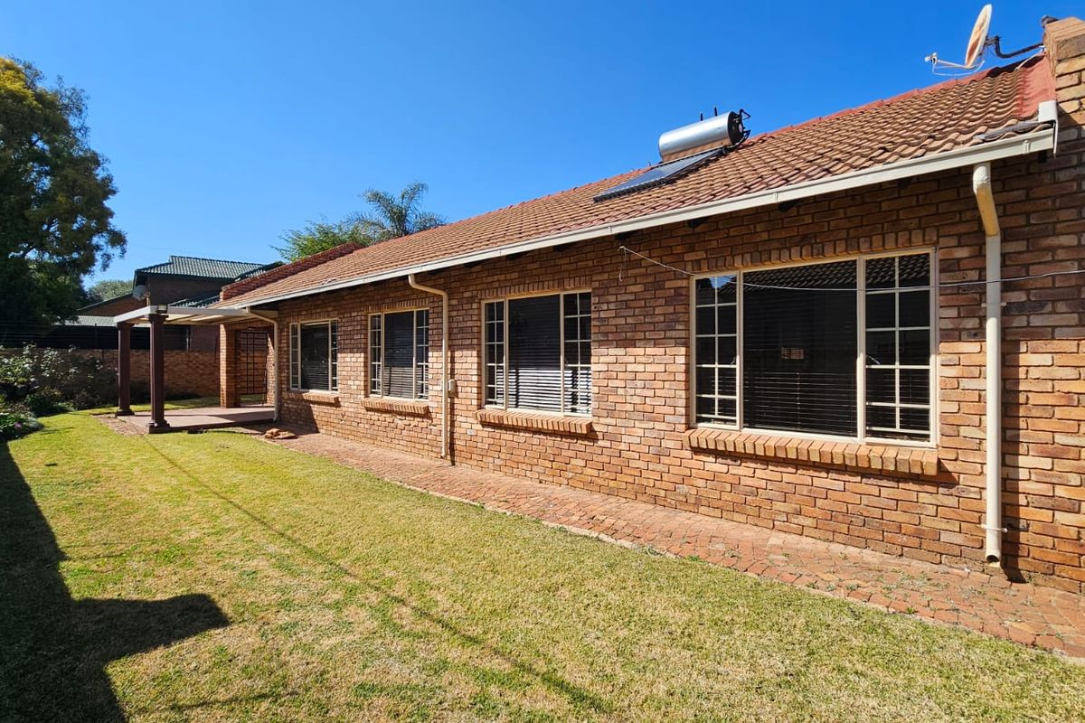 Rear view of a brick-faced house featuring a tiled roof, solar water heater, and a paved patio area overlooking the garden.