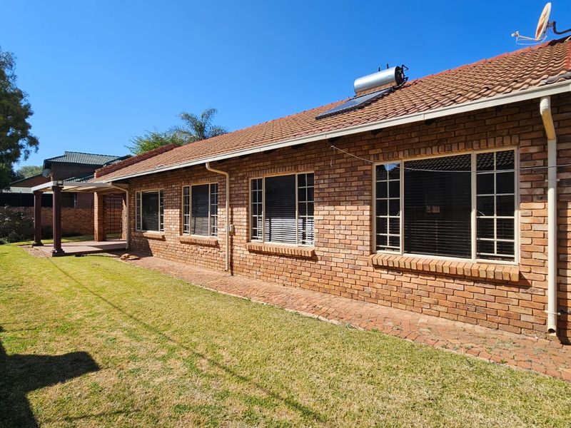 Rear view of a brick-faced house featuring a tiled roof, solar water heater, and a paved patio area overlooking the garden.