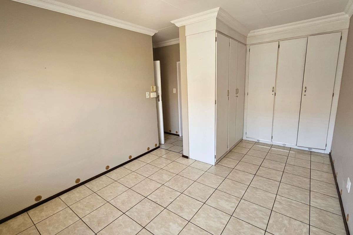A vacant bedroom featuring neutral walls, ceramic floor tiles, crown molding, and ample built-in cupboard storage space.