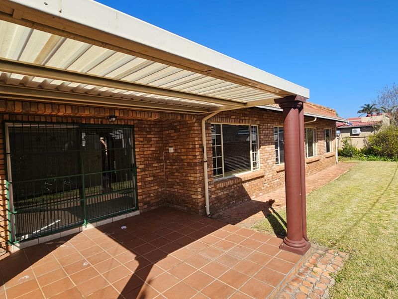 A covered brick patio area featuring tiled flooring and support columns, overlooking a private garden space.