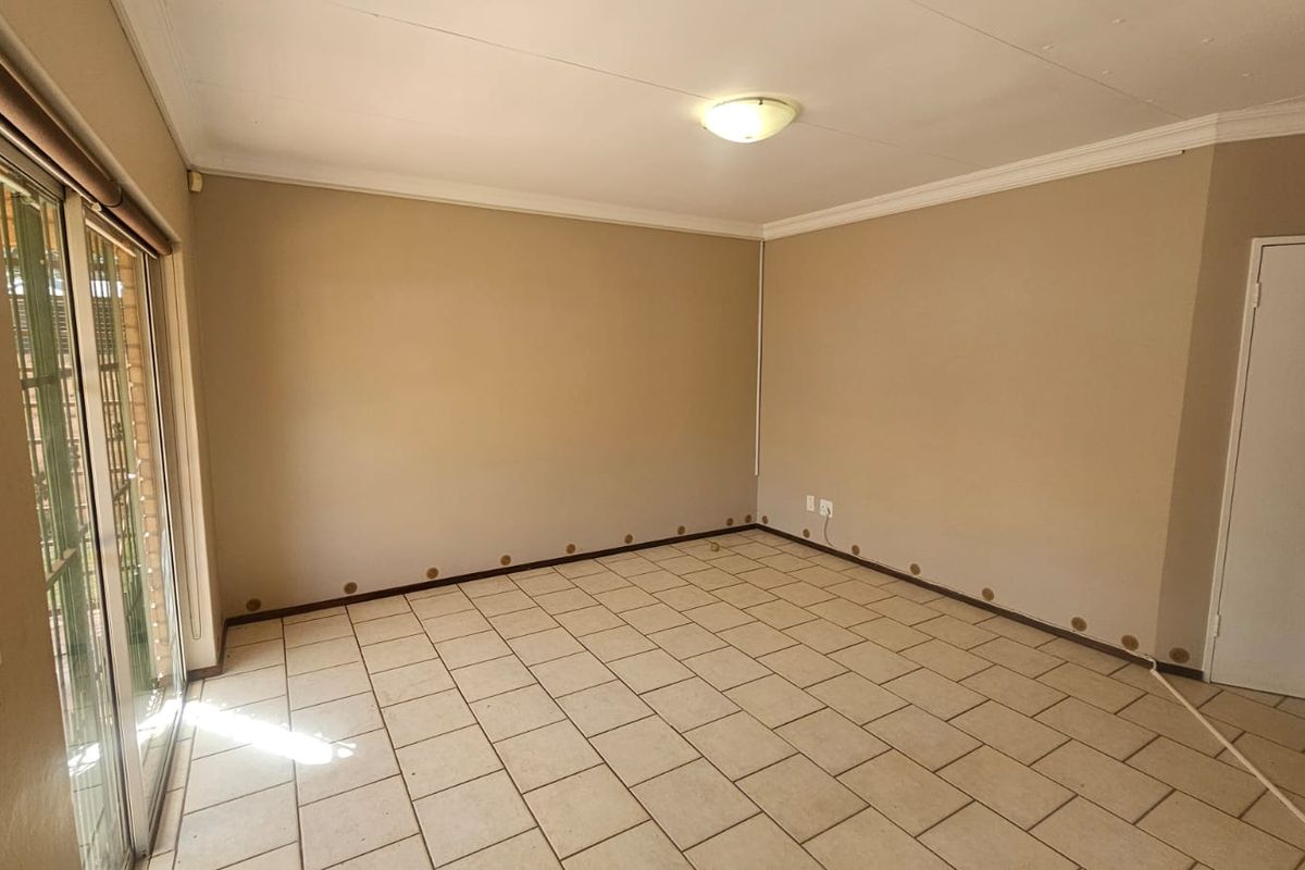 An empty living room featuring tiled flooring, a sliding glass door, and coved ceiling cornices, requiring minor cosmetic repairs to walls and baseboards.