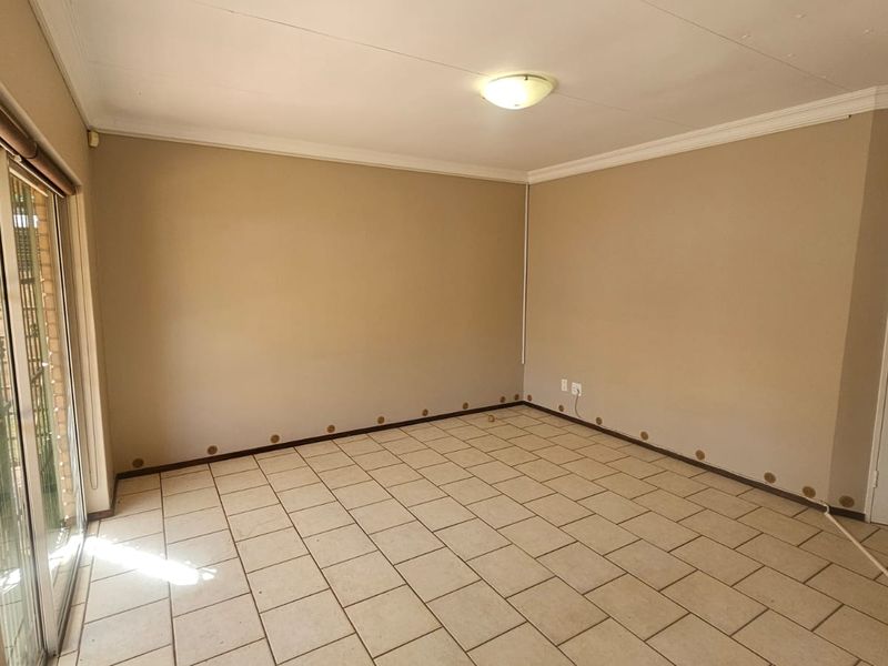 An empty living room featuring tiled flooring, a sliding glass door, and coved ceiling cornices, requiring minor cosmetic repairs to walls and baseboards.